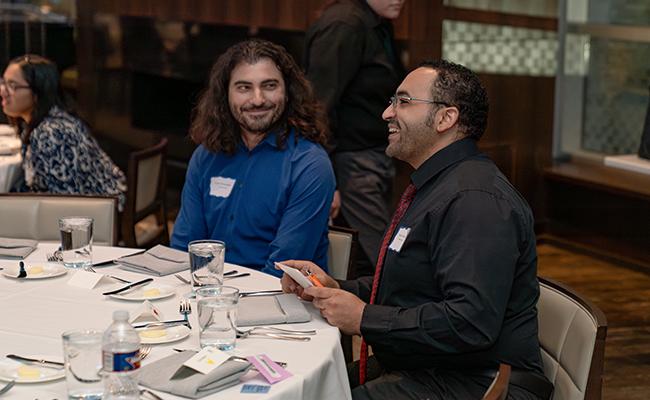 PhD students Eyad Shihabeddin and Elsayed Zaabout sitting at table talking at dinner.