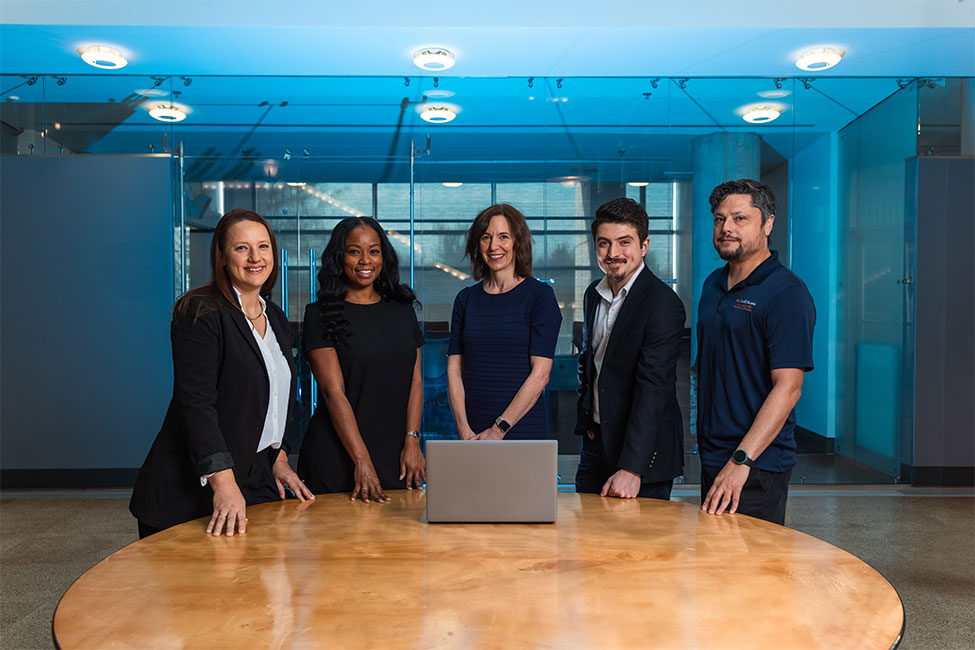 Five UTHealth Houston employees standing behind a table with a laptop on it