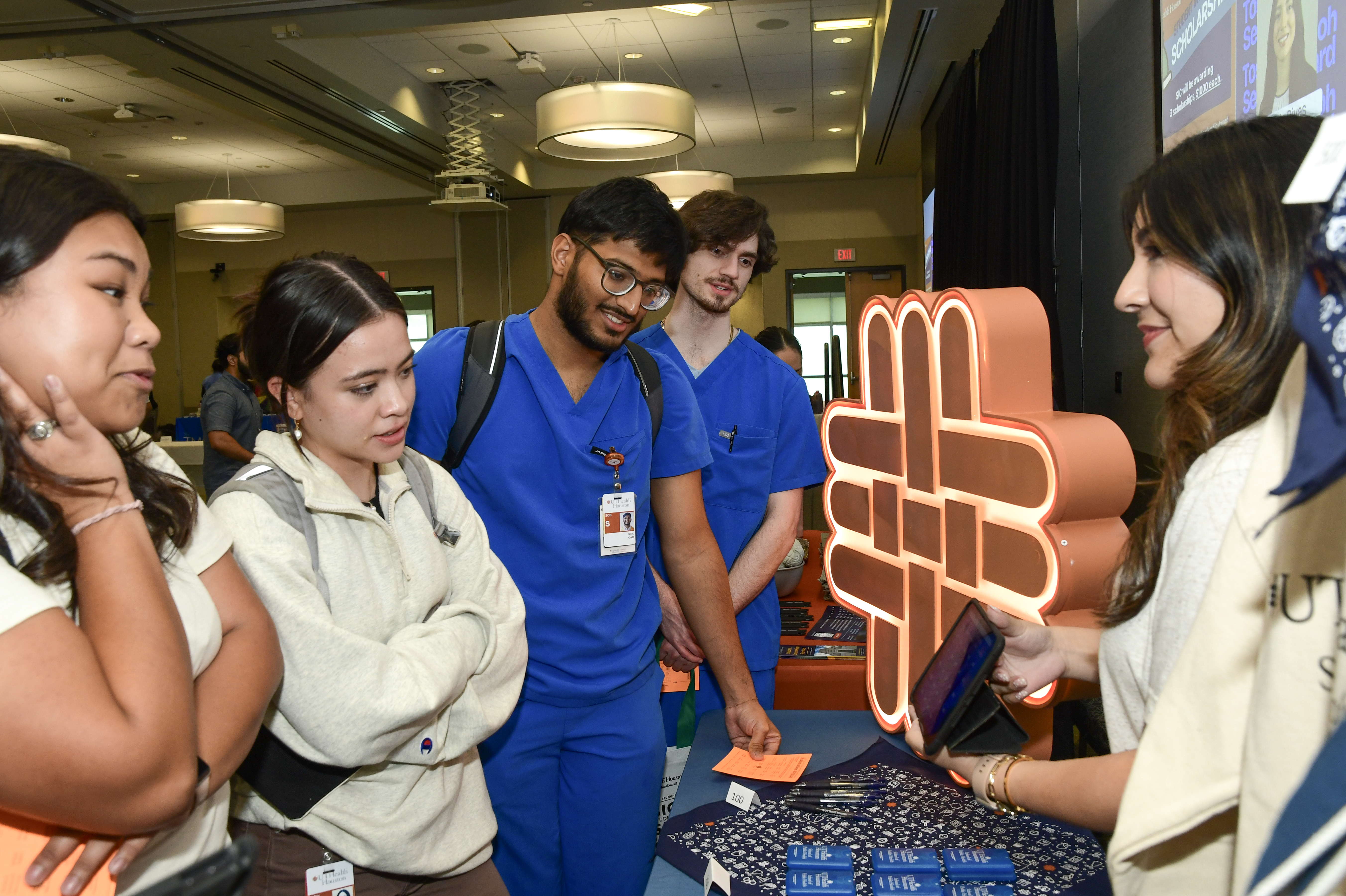 Five individuals, four students and one staff member, interact at a resource table at a student mixer event.